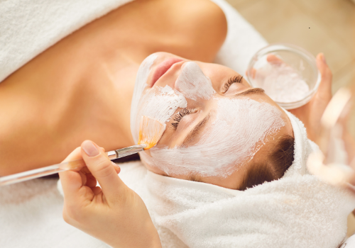 A woman receiving a skincare facial treatment, with a soothing mask being applied to her face, highlighting a professional skincare routine for hydration, anti-aging, and overall skin health.