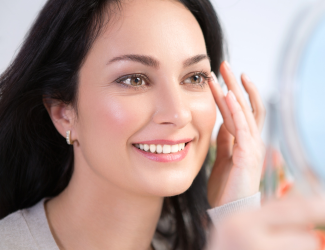 Woman applying skincare products to her face in a mirror, focusing on hydration and anti-aging skincare for youthful, radiant skin.