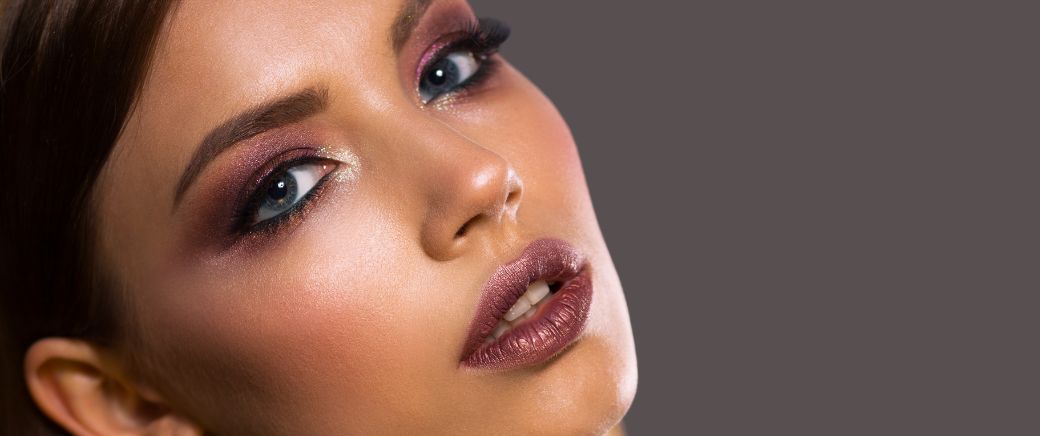 A model showcasing 2025 makeup trends with glowy skin, bold eyeliner, fluffy brows, and glossy lips, featuring sustainable and cruelty-free beauty products.