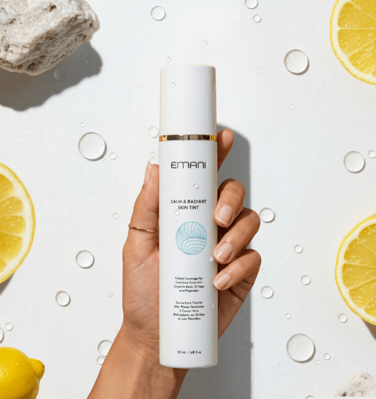 Hand holding a skincare product with lemons and water droplets on a light background | Calm & Radiant Skin Tint